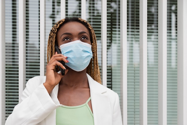 Junge schwarze Frau, die mit Handy spricht und eine Gesichtsmaske trägt Kopienraum Kommunikation