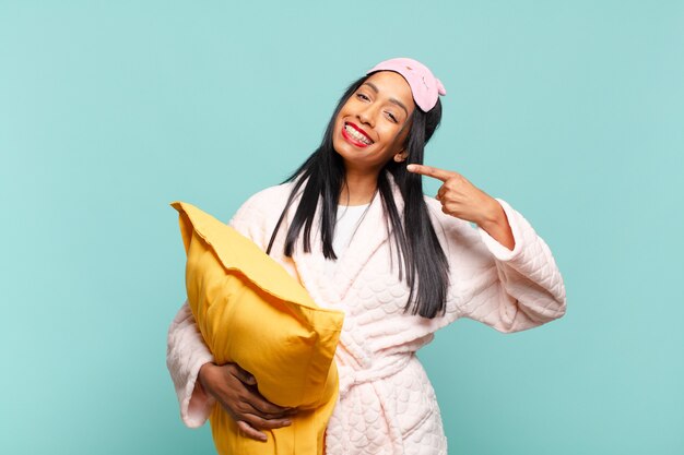 Junge schwarze Frau, die selbstbewusst lächelt und auf ihr eigenes breites Lächeln, positive, entspannte, zufriedene Haltung zeigt. Pyjama-Konzept