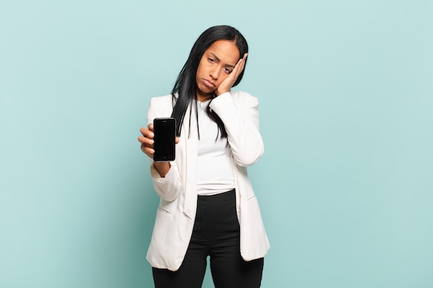 Junge schwarze Frau, die sich nach einer ermüdenden, langweiligen und mühsamen Aufgabe gelangweilt, frustriert und schläfrig fühlt und Gesicht mit Hand hält. Smartphone-Konzept