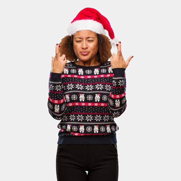 Junge schwarze Frau in einer modischen Weihnachtsstrickjacke mit den Drucküberfahrtfingern für das Glück haben