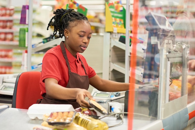 Junge schwarze Frau in Uniform scannt verpackte Lebensmittel von Käufern