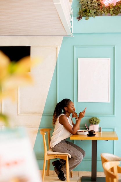 Junge schwarze Frau mit Handy beim Frühstück im Café