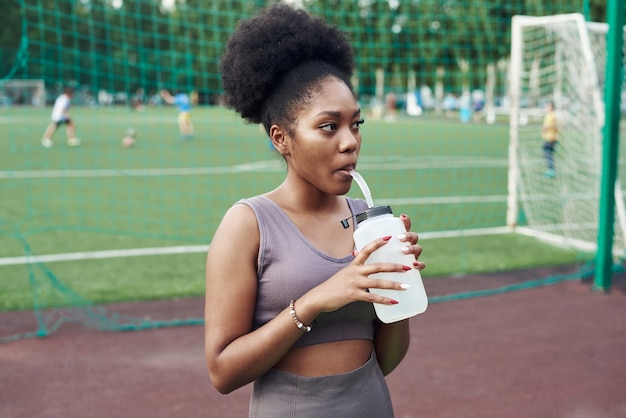 Junge schwarze Frau trinkt Wasser von einer Flasche am Stadion. Outdoor-Sportarten.