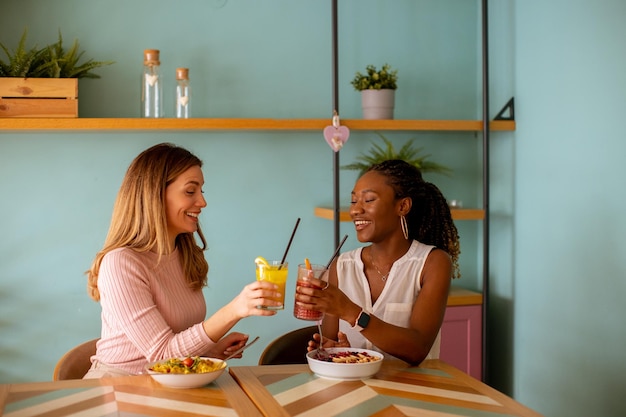 Junge schwarze und kaukasische Frau, die gute Zeit hat, frische Säfte zu trinken und im Café gesund zu frühstücken