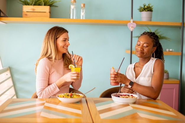 Junge schwarze und kaukasische Frau, die gute Zeit hat, frische Säfte zu trinken und im Café gesund zu frühstücken