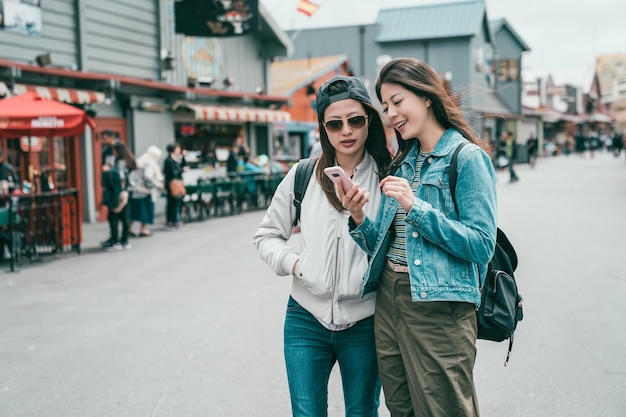 junge Schwestern, die Informationen über ein Handy auf der Straße einer ruhigen und schönen Stadt austauschen.