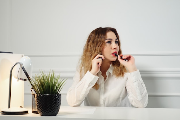 Junge Sekretärin mit lockigen Haaren telefoniert mit dem Kunden und macht sich Notizen am Tisch im Büro. Büroarbeitskonzept.