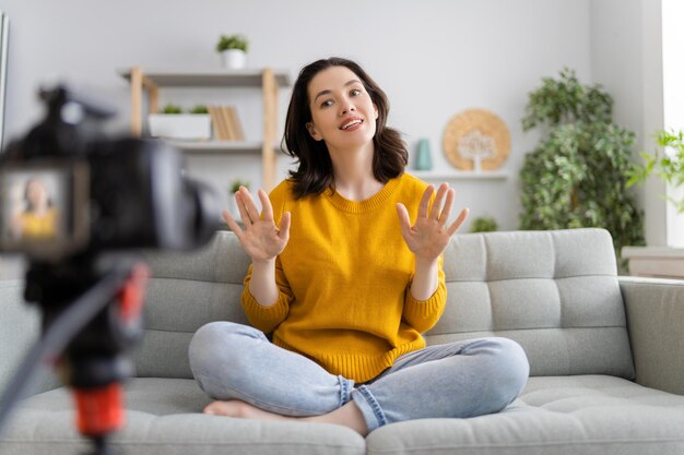 Junge selbstbewusste Frau spricht über Digitalkamera, die Vlog auf dem Sofa zu Hause aufnimmt.