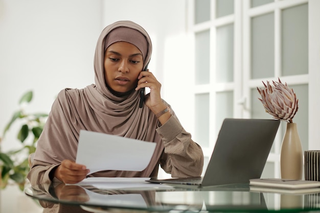 Junge, selbstbewusste Geschäftsfrau im Hijab berät einen Kunden über ein Smartphone