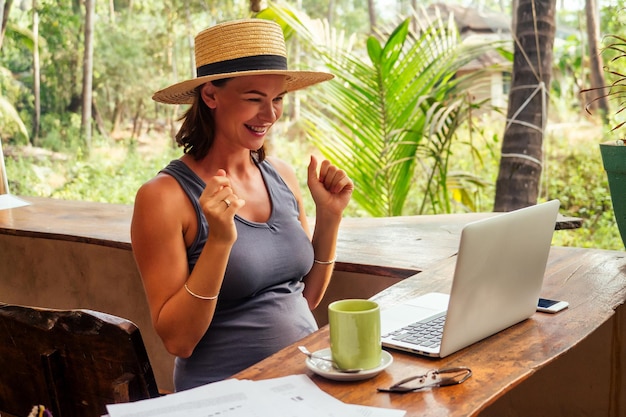 Junge, selbstbewusste, hübsche Frau, die mit Laptop und Kreditkarte im tropischen Sommercafé am Strand arbeitet