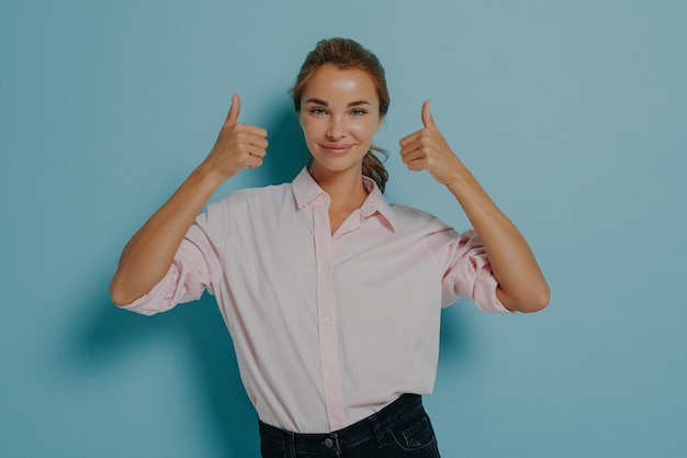 Junge selbstbewusste, unterstützende, glückliche junge Dame zeigt Daumen hoch mit beiden Händen