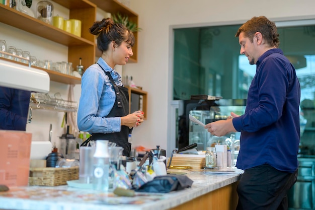 Junge serviceorientierte Barista-Frau mit Kunden im Café