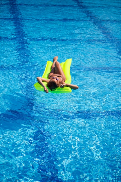 Junge sexy Frau in einem Badeanzug schwimmt im Pool auf einer aufblasbaren Matratze. Mädchen mit Sonnenbrille in einem blauen Pool im Urlaub