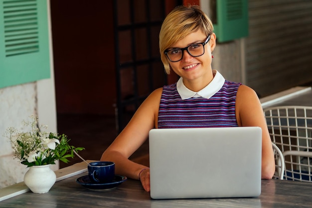 Junge sexy Frau in einem stylischen Hemd mit Laptop und Telefon freiberuflich am tropischen Paradiesstrand Mädchen Tasse Tee Kaffee Freiberuflerin Arbeit sitzend in einem Sommercafé Fernarbeit Indischer Ozean