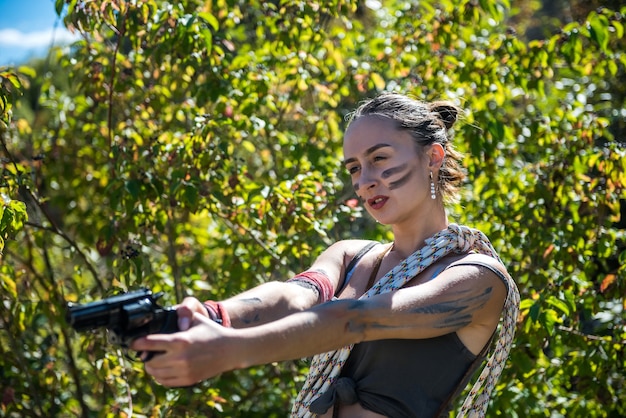 Junge sexy Jägerin mit Top und Shorts, die eine Waffe in der Natur hält