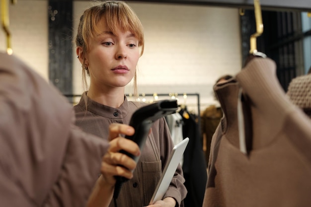 Foto junge shop-assistentin mit tablet und scanner, die informationen überprüft