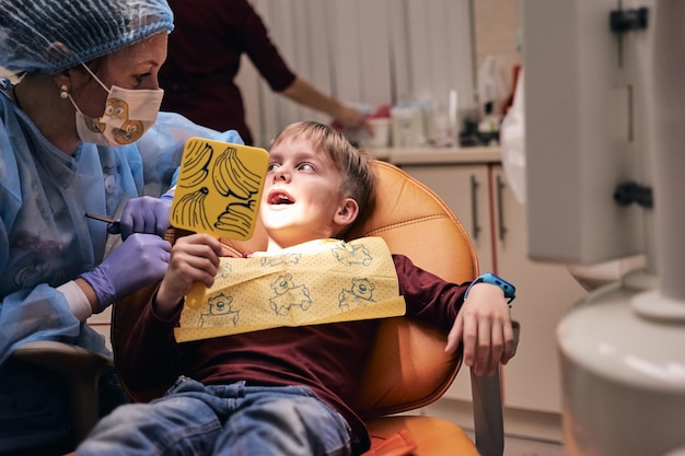 Junge sitzt auf dem Zahnarztstuhl mit offenem Mund während der mündlichen Untersuchung mit dem Arzt. Besuch in der Kinderzahnheilkunde.