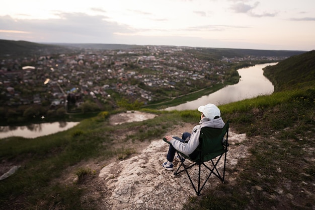 Junge sitzt auf einem Stuhl und wandert im Urlaub, macht ein abendliches Picknick auf dem Gipfel des Berges und blickt auf die wunderschöne Canyon-Landschaft