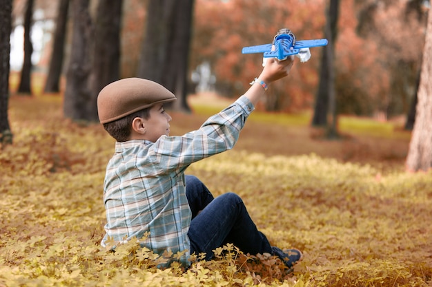 Junge sitzt im Wald und spielt mit einem Spielzeugflugzeug