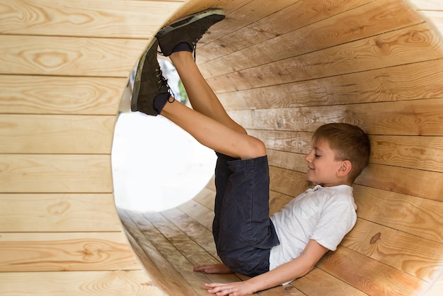 Junge sitzt in einem Holztunnel Öko-Spielplatz für Kinder