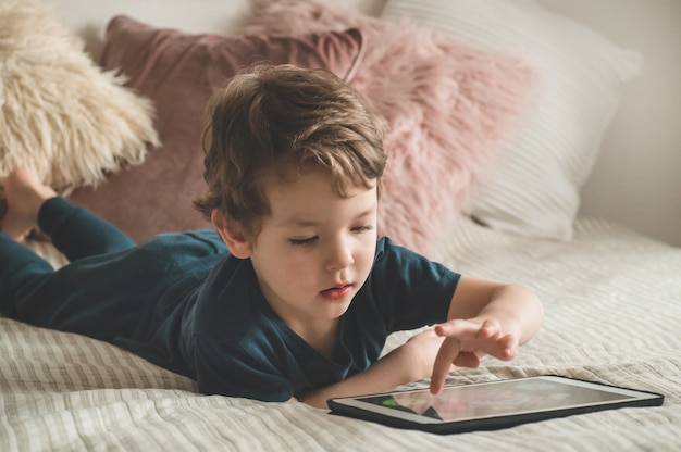 Junge sitzt mit einer Tablette auf dem Bett