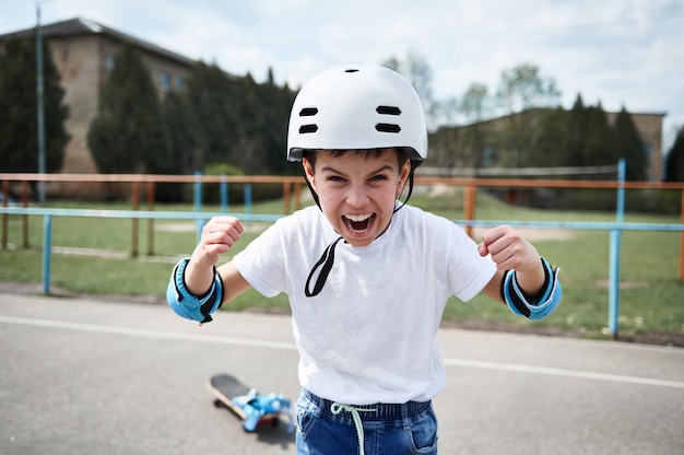 Junge Skateboarder im Schutzhelm schreit und zeigt Fäuste, die nach vorne schauen