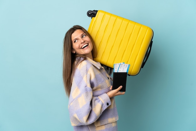 Junge slowakische Frau lokalisiert auf blauer Wand im Urlaub mit Koffer und Pass