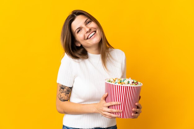 Junge slowakische Frau lokalisiert auf Gelb hält einen großen Eimer Popcorn