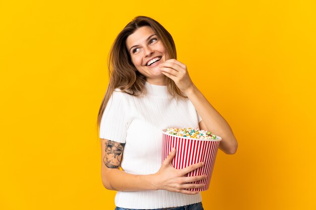 Junge slowakische Frau lokalisiert auf gelber Wand, die einen großen Eimer Popcorn hält