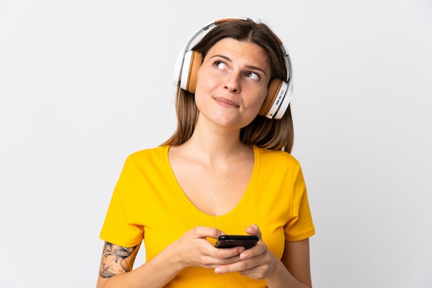 Junge slowakische Frau lokalisiert auf weißem Hintergrund, der Musik mit einem Handy und Denken hört