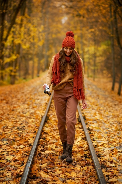 Junge Smiley-Fotografin, die mit der Kamera im Herbstpark mit Eisenbahn spazieren geht. Romantische Herbstzeit