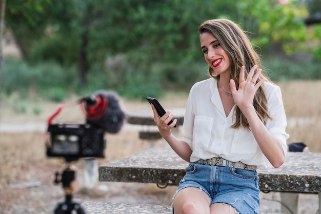 Junge spanische Bloggerin benutzt ihr Telefon und nimmt sich mit einer DSLR-Kamera in einem Park auf