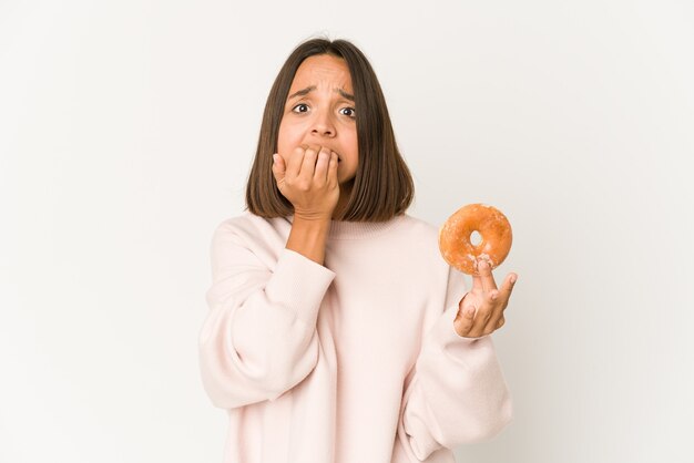 Junge spanische Frau, die einen Donut isst, der Fingernägel beißt, nervös und sehr ängstlich.