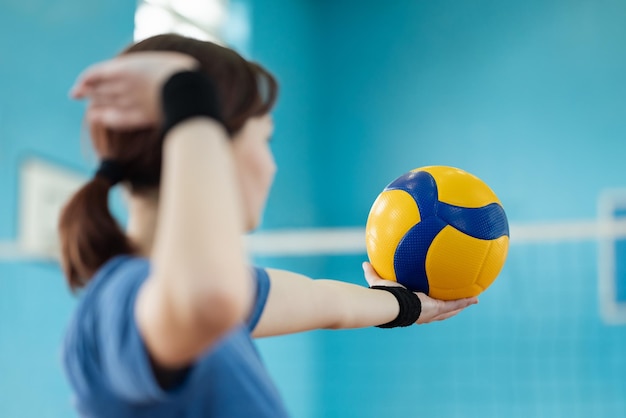 Junge Spielerin bereitet sich darauf vor, den Volleyball auf der gegnerischen Seite des Netzes aufzuschlagen. Weibliche Lernende erlernen Fähigkeiten im Volleyball-Übungsaufschlag