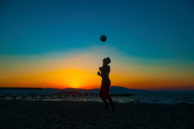 Junge spielt Fußball am Strand bei Sonnenuntergang