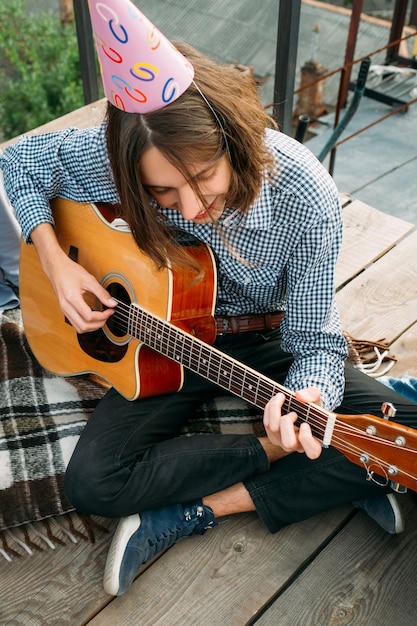 Junge spielt Gitarre und singt alles Gute zum Geburtstag mit einem Partyhut. Musikalische Gratulation. Feierspaß