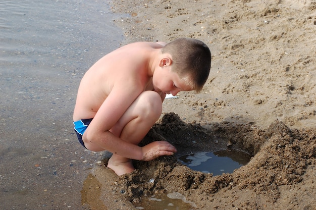 Junge spielt mit Sand an der Küste