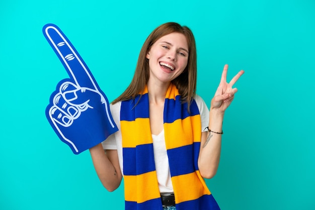 Junge Sportfanfrau isoliert auf blauem Hintergrund, lächelnd und Victory-Zeichen zeigend