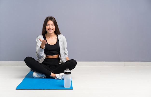 Junge Sportfrau, die auf dem Boden mit dem Mattenhändeschütteln nach viel sitzt