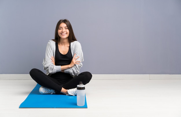 Junge Sportfrau, die auf dem Boden mit dem Mattenlachen sitzt