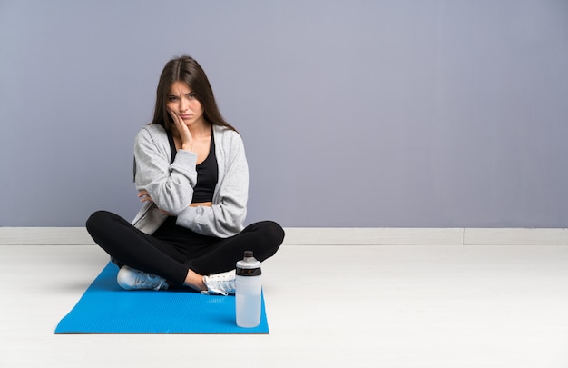 Junge Sportfrau, die auf dem Boden mit der Matte unglücklich und frustriert sitzt