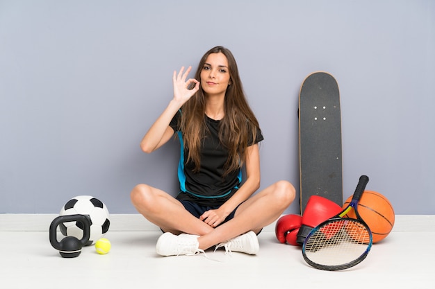 Foto junge sportfrau, die auf dem boden zeigt ein okayzeichen mit den fingern sitzt