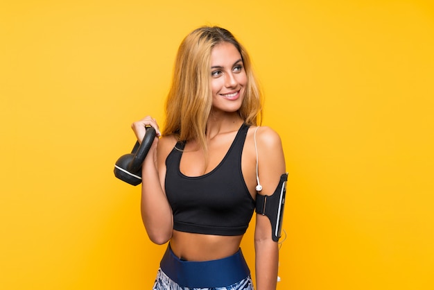 Junge Sportfrau, die das Gewichtheben mit kettlebell über lokalisierter gelber Wand macht