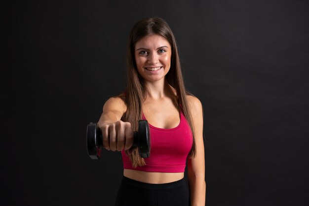 Junge Sportfrau, die das Gewichtheben über lokalisiertem schwarzem Hintergrund macht