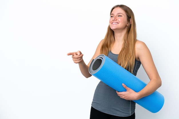 Junge Sportfrau, die zu Yoga-Kursen geht, während sie eine Matte hält, die mit dem Finger zur Seite zeigt und ein Produkt präsentiert