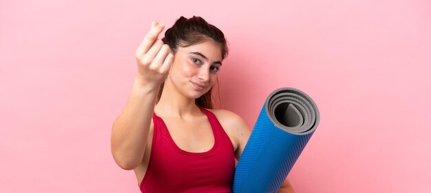 Foto junge sportfrau, die zu yogakursen geht, während sie eine matte hält, die geldgeste macht