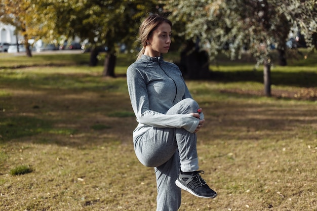 Junge Sportfrau im Sportanzug wärmt sich im Herbstpark auf