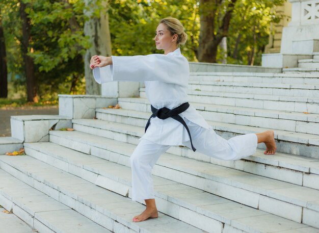 Junge Sportfrau in einem weißen Kimono mit einem schwarzen Gürtel macht ein Aufwärmen auf der Treppe vor dem Training. Kampfkunst, Selbstverteidigung