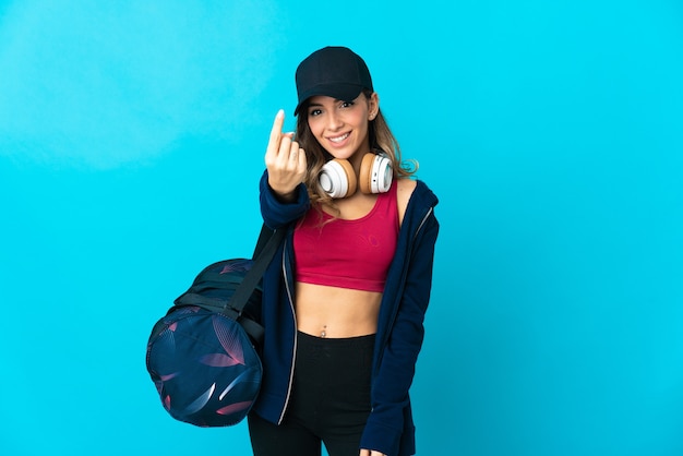 Junge Sportfrau mit Sporttasche lokalisiert auf blauem Hintergrund, der kommende Geste tut