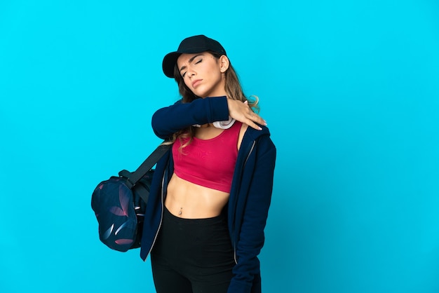 Junge Sportfrau mit Sporttasche lokalisiert auf blauer Wand, die unter Schmerzen in der Schulter leidet, weil sie sich bemüht hat